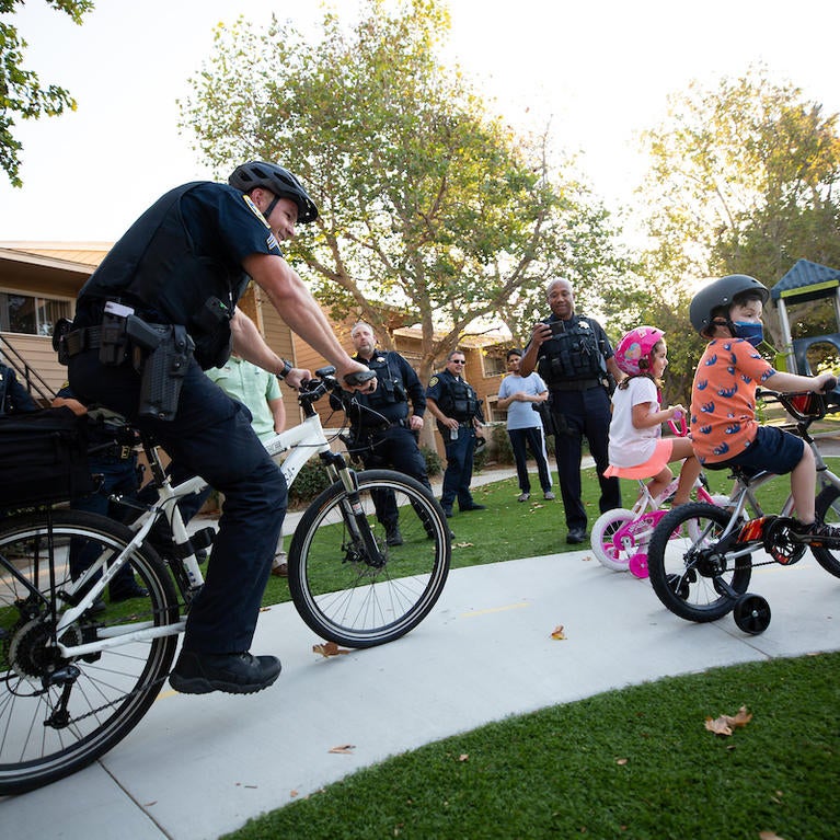Police officer Paul Dombrowski, with the University of California Riverside Police Department, rides with Jet Wilbur, 6, front, and Claire Canale, 4, as they both ride donated bicycles at the Oban Family Housing at UC Riverside on Friday, September 17, 2021. Officer Dombrowski helped raise money from the department’s officers and staff to purchase the bikes for the children. (UCR/Stan Lim)