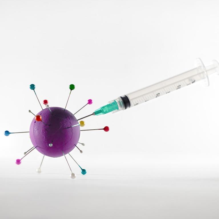 A syringe injecting a vaccine into a ball with pins that represents the covid-19 virus