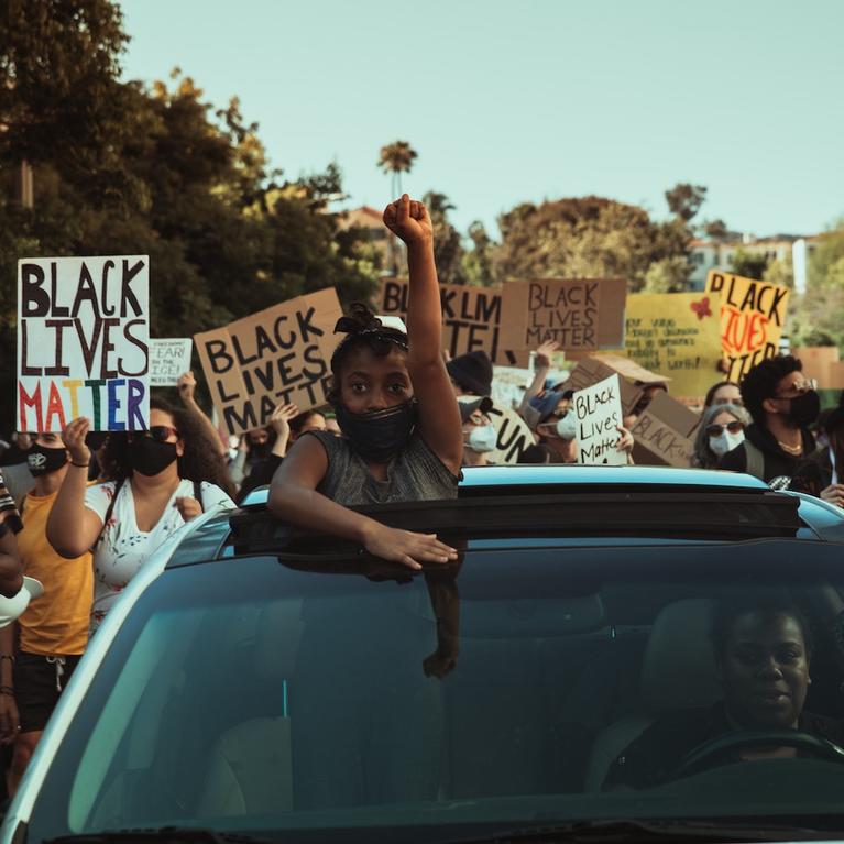 A girl raises her fist from the roof of a car at a Black Lives Matter protest